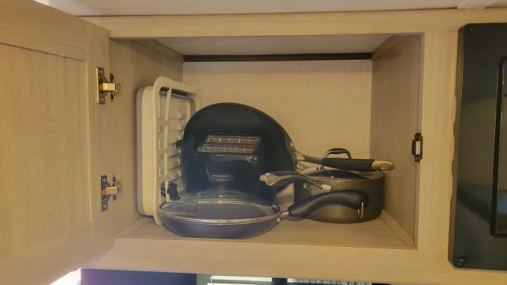 Open cabinet in an RV rental, revealing a toaster, frying pans, and saucepans neatly stored for kitchen use.. Crossroads RV Sunset Trail 2026