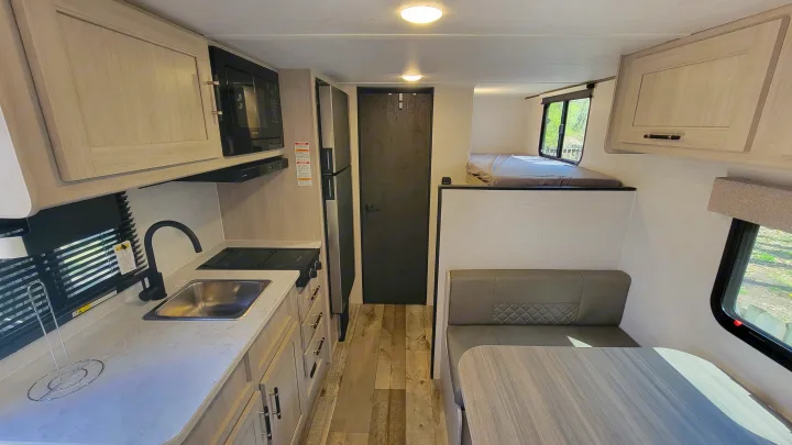 Compact rv rental interior with kitchen (sink, stovetop, microwave, fridge), dinette, and raised bed.. Crossroads RV Sunset Trail 2026