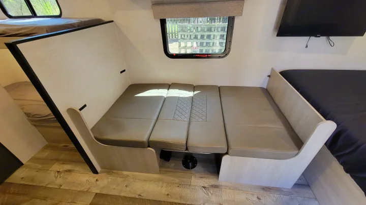 RV rental interior: A light-toned dinette area converts to a bed, flanked by bunk beds (left) and another bed with TV (right).. Crossroads RV Sunset Trail 2026