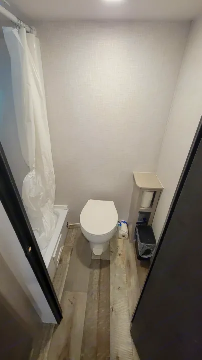 Compact RV rental bathroom featuring a toilet, shower with curtain, and narrow shelving for essentials.. Crossroads RV Sunset Trail 2026