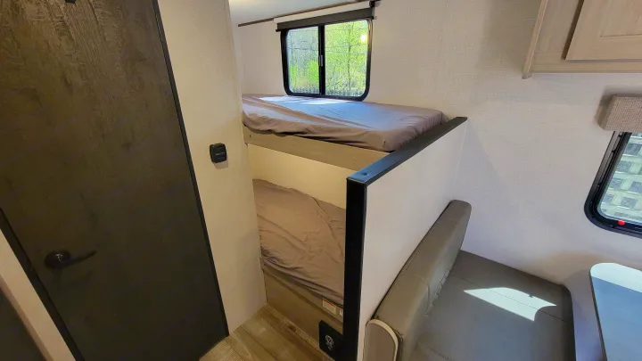 RV rental interior with stacked bunk beds and a dinette seating area, offering cozy lodging for family trips.. Crossroads RV Sunset Trail 2026