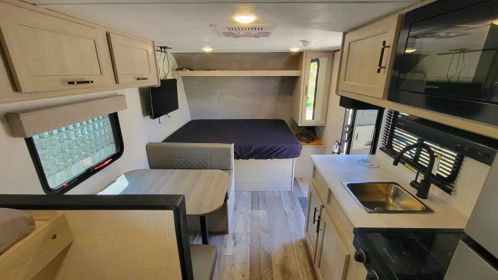 Interior of an rv rental featuring a bed, dinette, and kitchen with light wood cabinetry, sink, and microwave. Ready for adventure.. Crossroads RV Sunset Trail 2026
