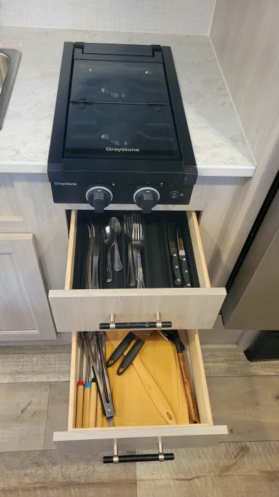 RV rental kitchen featuring a Greystone stovetop & open drawers with silverware & cooking utensils for easy access.. Crossroads RV Sunset Trail 2026