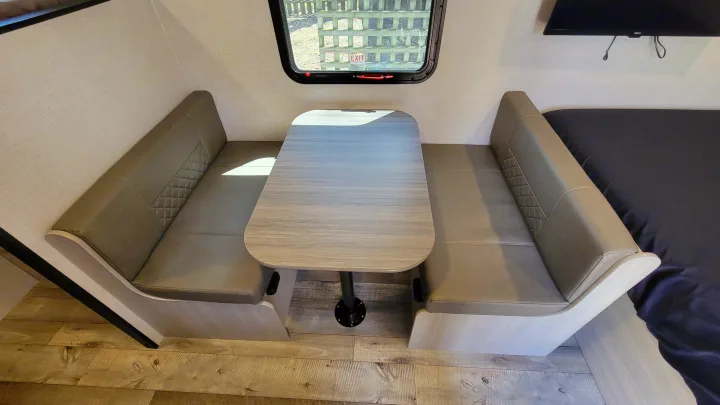 RV rental interior features a dinette with two gray, quilted benches, a light wood table, and window views.. Crossroads RV Sunset Trail 2026