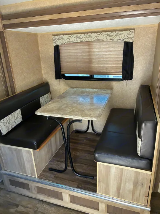 Step inside this RV rental's dinette area, featuring black leatherette benches, a marbled table, and a window with blinds.. Coachmen Catalina Sumit Series 2019