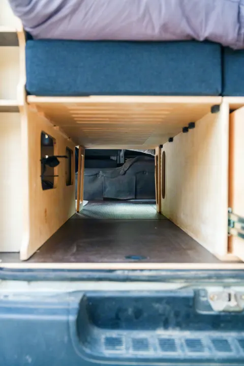 RV rental storage view: Wooden bed frame & under-bed storage tunnel inside a van, ideal for campervan adventures.. Toyota Hiace 2005