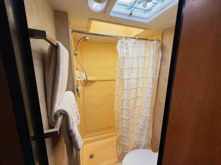 Experience convenience in this rv rental's compact bathroom, featuring a shower with curtain, toilet, and fresh towels.. Thor Majestic 2013