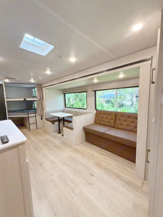 Modern RV rental interior with light wood floors, bunk beds, a dinette, and a comfy sofa. Ideal for family adventures.. Forest River Surveyor Legend X 2025