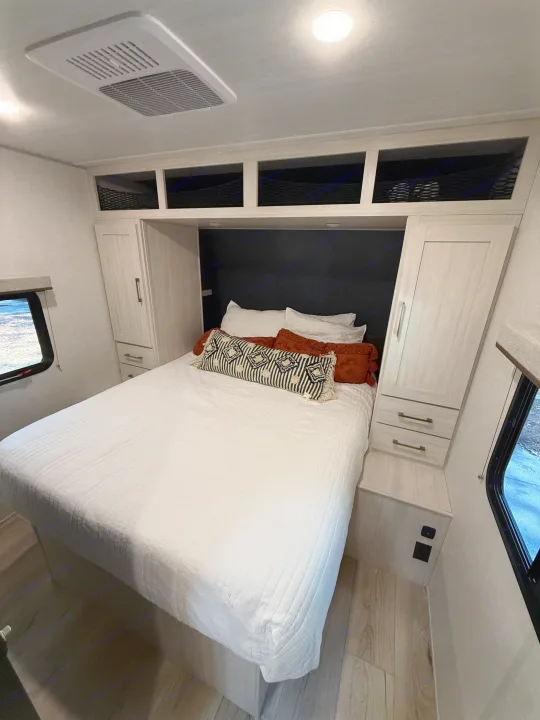 This modern RV rental bedroom offers a comfortable queen bed, ample storage in light wood-look cabinetry, and overhead AC.. Forest River Surveyor Legend X 2025