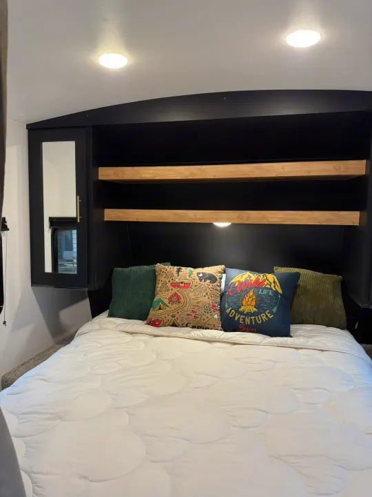 Cozy RV rental bedroom featuring a comfortable bed with decorative throw pillows, built-in shelving, and a mirrored wardrobe.. Keystone RV Springdale 2022