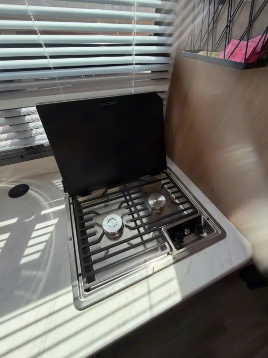 RV rental kitchen: modern two-burner Dometic gas stove, sink area, and window blinds with sunlit countertops.. Thor Vegas 2026