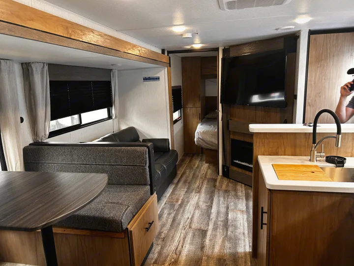 Spacious RV rental interior featuring a cozy dinette, kitchen with sink, living area with TV/fireplace, and partial bedroom view.. Forest River Campsite Reserve 2024