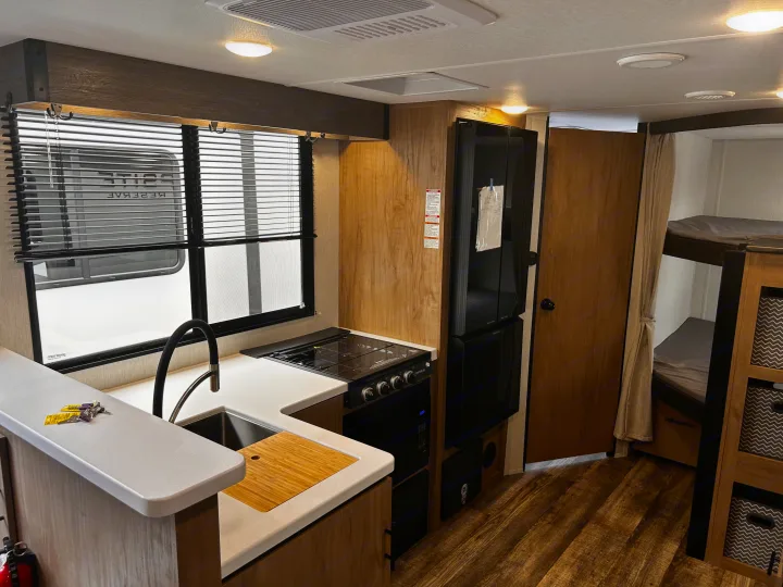 This rv rental offers a functional kitchen with sink, stove, microwave, and refrigerator, plus bunk beds.. Forest River Campsite Reserve 2024