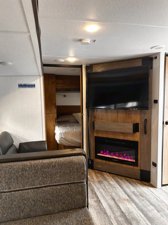Modern rv rental interior: A cozy living space with a wall-mounted TV, electric fireplace, and a glimpsed bunk bed area.. Forest River Campsite Reserve 2024