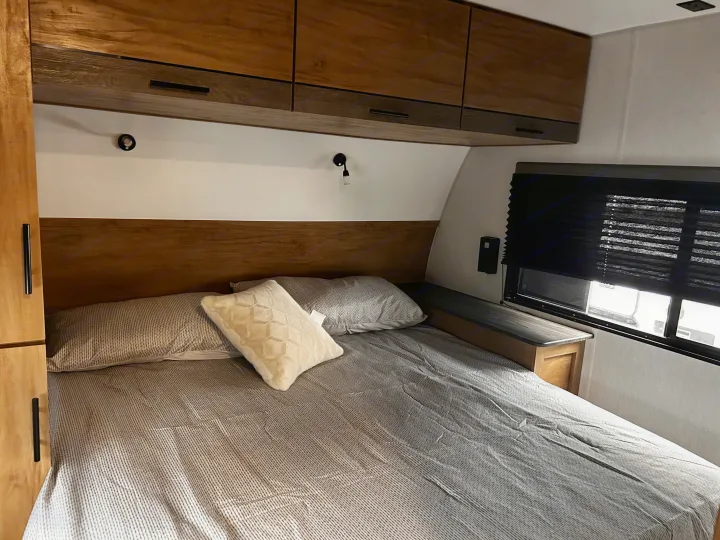 RV rental bedroom: comfy bed, wooden overhead storage, and window with blackout blinds for a good night's sleep.. Forest River Campsite Reserve 2024