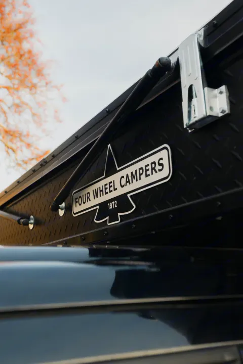 Side of a black Four Wheel Campers pop-up truck camper, featuring diamond plate texture. Great for your next rv rental trip!. Ford F350 2025