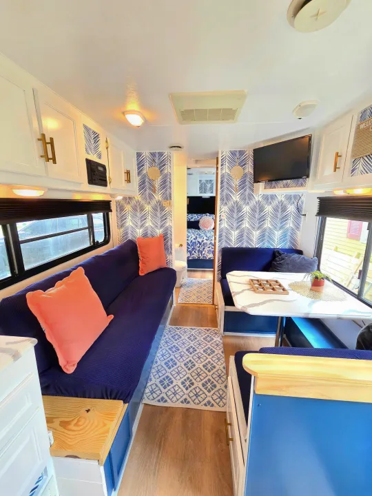 Updated rv rental living space: blue sofa with pink pillows, a dinette, patterned blue & white walls, wood floors.. Sunline Solaris 2002