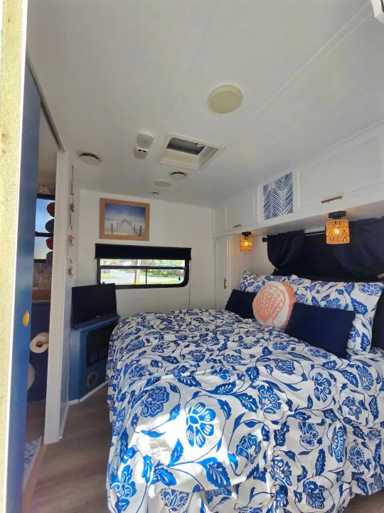 Cozy RV rental bedroom with blue and white floral bedding, coastal decor, and a small TV. Perfect for your next adventure!. Sunline Solaris 2002