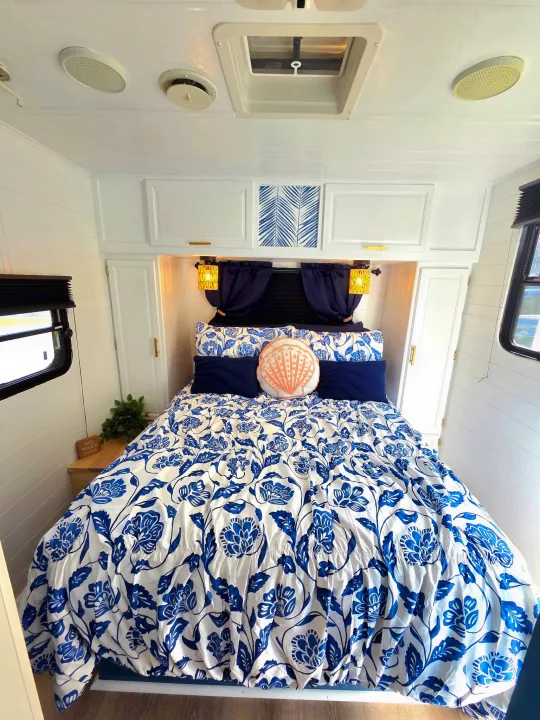 This bright RV rental bedroom features a comfy bed with blue floral bedding, shiplap walls, and modern decor.. Sunline Solaris 2002