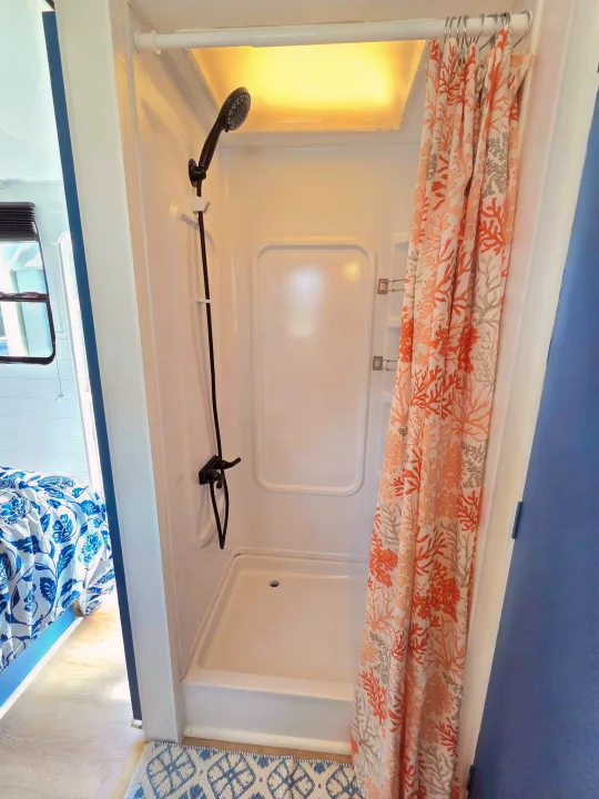 Compact RV rental shower with a vibrant coral curtain, modern black fixtures, and overhead skylight. View of bed and window.. Sunline Solaris 2002
