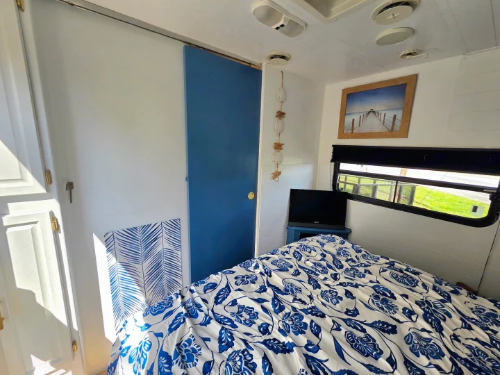 Cozy RV rental bedroom featuring blue floral bedding, a sliding door, and coastal decor. Ideal for a comfortable travel stay.. Sunline Solaris 2002