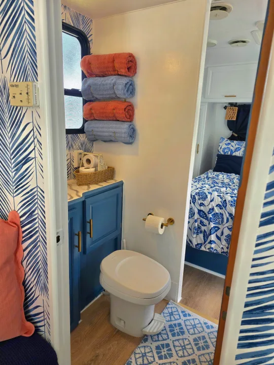 Stylish RV rental: blue bathroom with palm wallpaper, coral/blue towels, and a peek at the cozy floral-patterned bedroom.. Sunline Solaris 2002