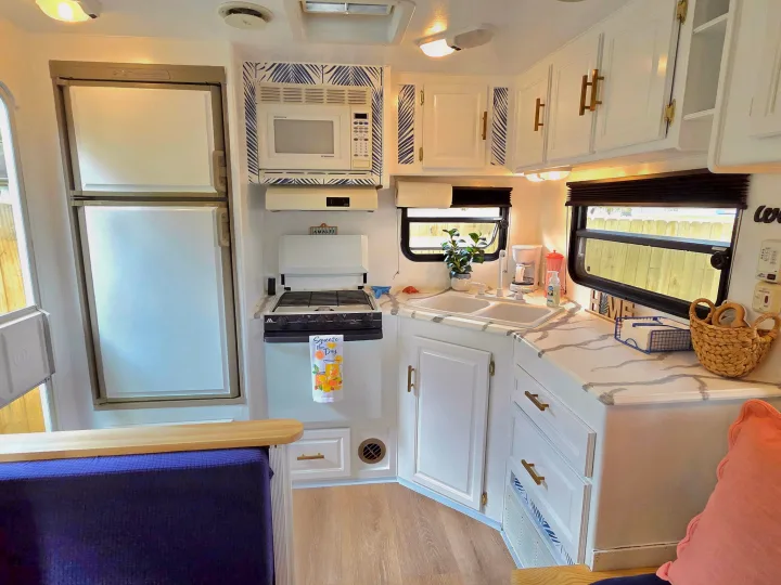 Bright rv rental kitchen featuring white cabinets, microwave, fridge, stove, sink, and blue accents for a modern feel.. Sunline Solaris 2002