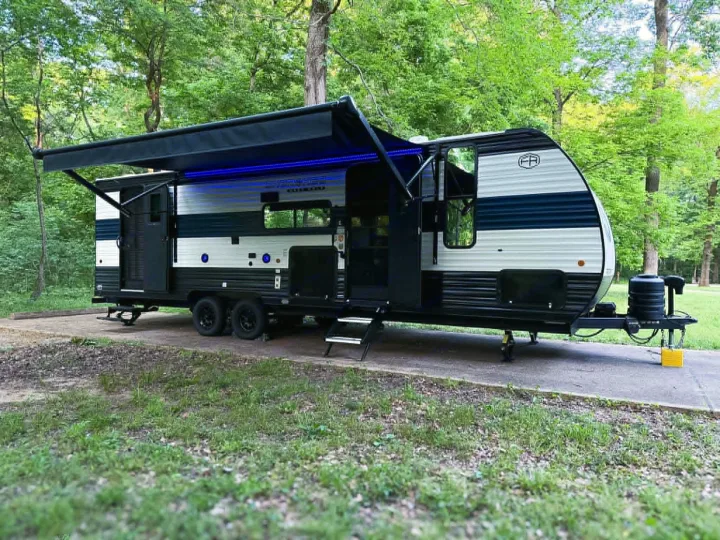 Black & white Forest River rv rental travel trailer at a wooded campsite with awning & blue LED lights.. Forest River Cherokee Grey Wolf 2025