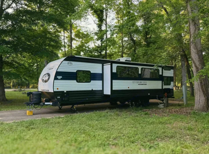 This RV rental, a white and black travel trailer, is nestled in a serene, treed campsite, ready for your adventure.. Forest River Cherokee Grey Wolf 2025