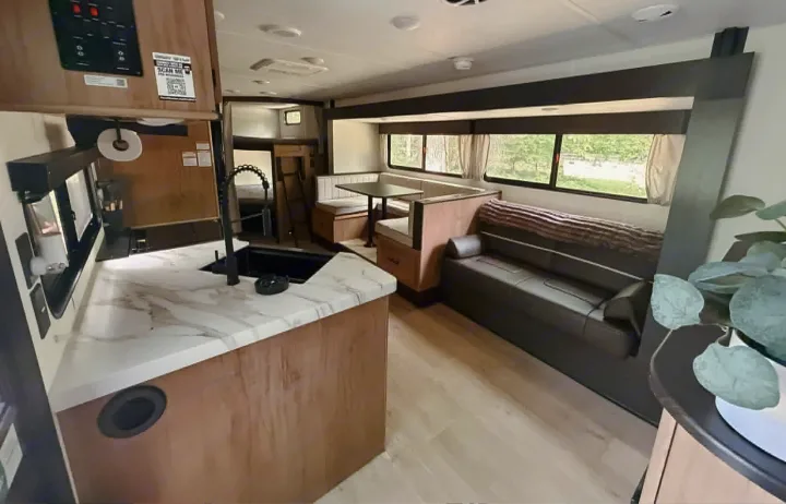 Modern RV rental interior with a kitchen counter & sink, dining booth, and living area sofa near scenic windows.. Forest River Cherokee Grey Wolf 2025