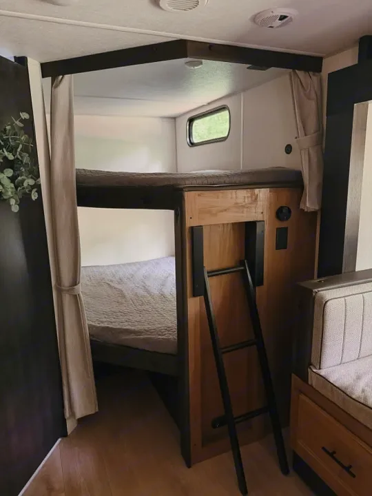 This rv rental features a cozy bunk bed area with a ladder, privacy curtains, and a window, designed for comfortable sleeping.. Forest River Cherokee Grey Wolf 2025