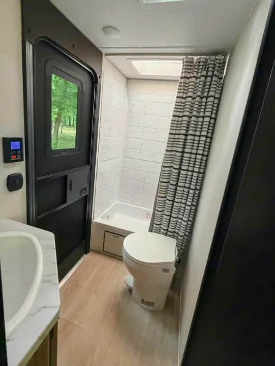 Compact and functional RV rental bathroom with shower, toilet, sink, and a view of nature through the door.. Forest River Cherokee Grey Wolf 2025
