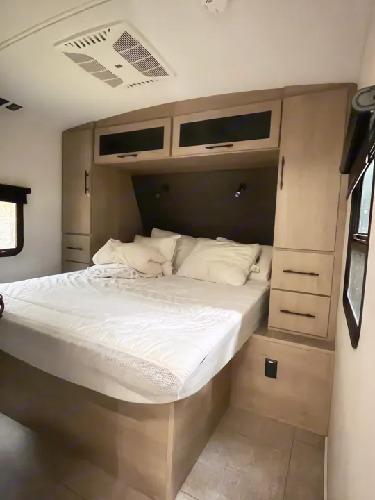 Cozy RV rental bedroom featuring a comfortable bed with white bedding, built-in storage, and an overhead AC unit.. Grand Design Imagine 3100RD 2025