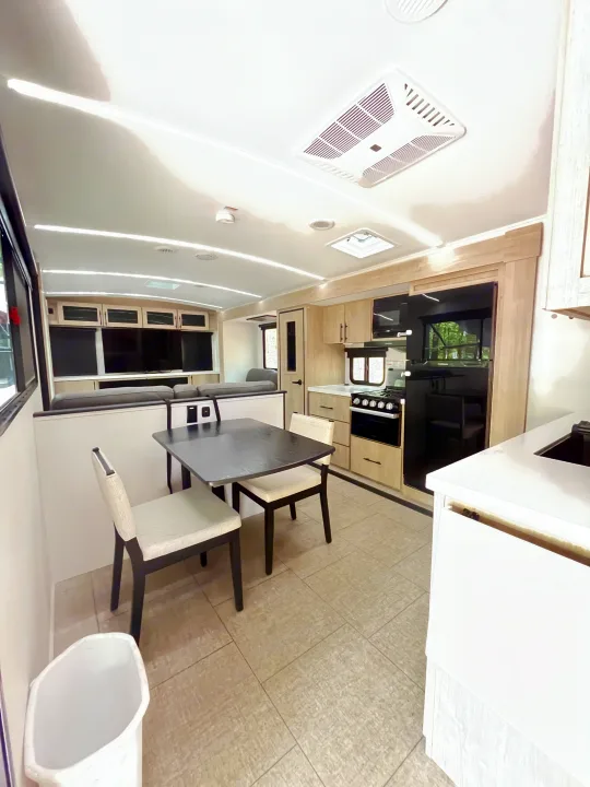 Modern RV rental interior featuring a kitchen with stove/fridge, dining table, and lounge area with TVs. Bright, tiled floors.. Grand Design Imagine 3100RD 2025