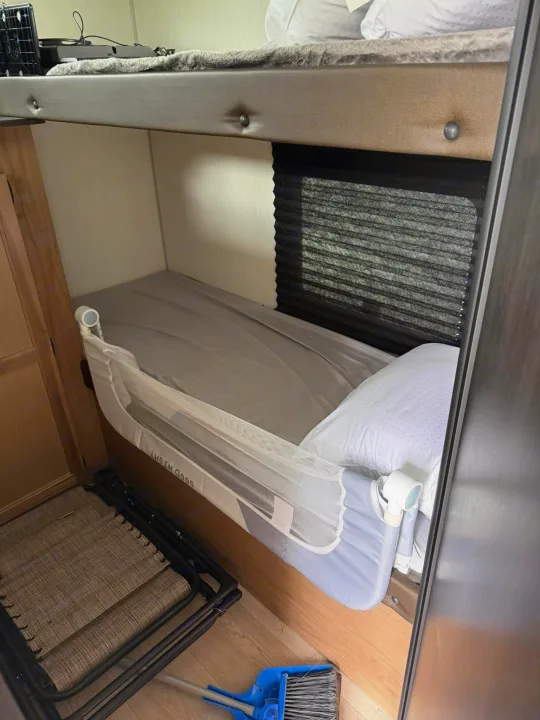 Inside an RV rental: a lower bunk bed with a child safety rail, an upper bunk, folded chairs, and cleaning tools on the floor.. Forest River Cherokee Grey Wolf 2025