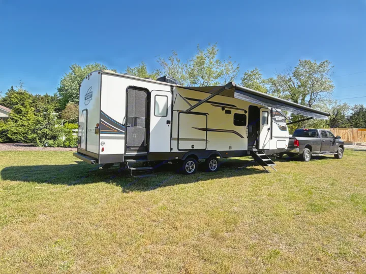 White travel trailer with extended awning, hitched to a pickup truck on a sunny, grassy day. Ideal for an RV rental getaway.. Coachmen 2963BH 2023