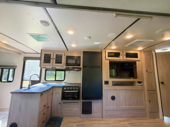 Modern RV rental kitchen and living area with light wood cabinets and essential appliances.. Coachmen 2963BH 2023
