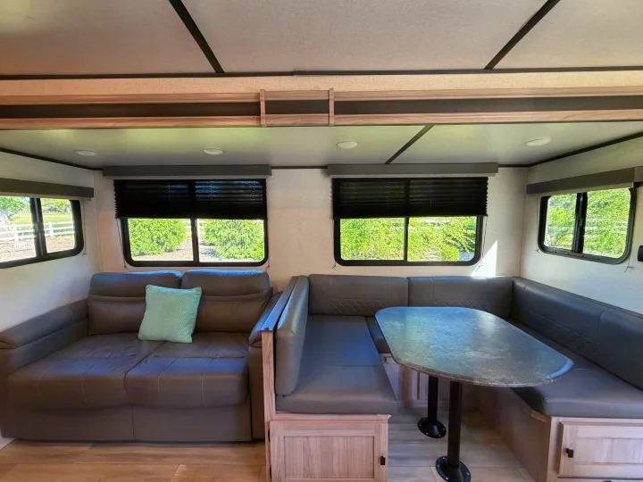 RV rental interior: comfy gray couch, U-shaped dinette with table, and bright windows for travel comfort.. Coachmen 2963BH 2023