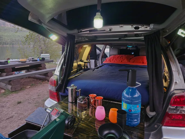 Car camping setup with bed, cooking gear, and scenic lake view. A clever alternative to an rv rental.. Toyota Highlander 2004