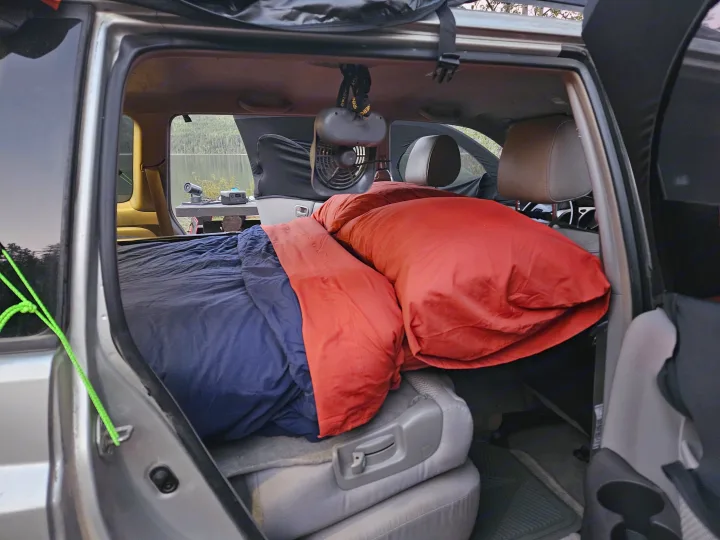 Car camping setup inside an SUV, offering a cozy sleeping space with lake views. A practical alternative to an RV rental.. Toyota Highlander 2004