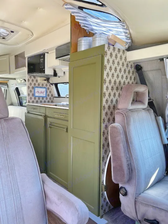 This RV rental interior showcases a charming kitchenette with green cabinets, patterned accents, and comfy front seats.. Roadtrek 190 Popular 1995