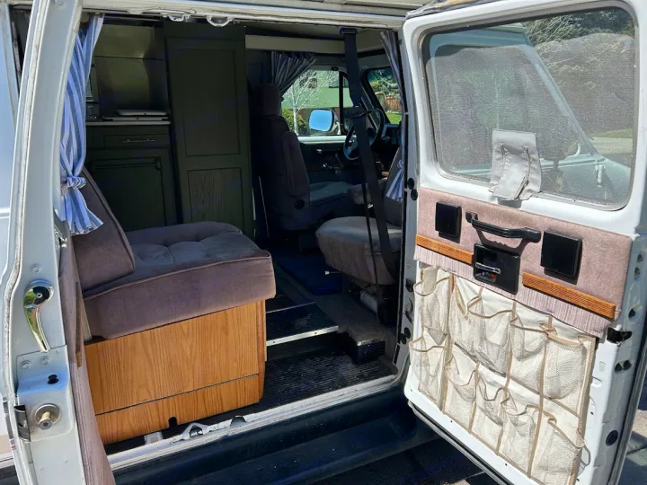 Cozy camper van RV rental interior: view through the open side door showing a bench seat, kitchenette, and door storage.. Roadtrek 190 Popular 1995