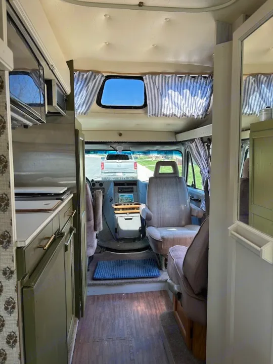 RV rental interior view: kitchenette with olive cabinets, cockpit, front seats, and a truck outside. Cozy camper van.. Roadtrek 190 Popular 1995