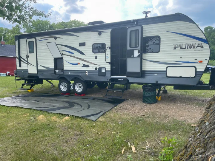 Puma travel trailer set up at a campsite. This RV rental features an outdoor mat and extended steps for easy access.. Forest River Palomino Puma 2019
