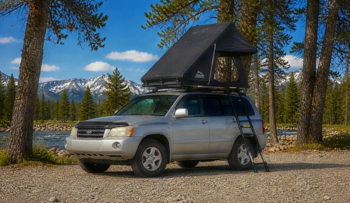 Scenic RV rental: Toyota Highlander with rooftop tent parked by a river & mountains, ready for adventure.. Toyota Highlander 2003