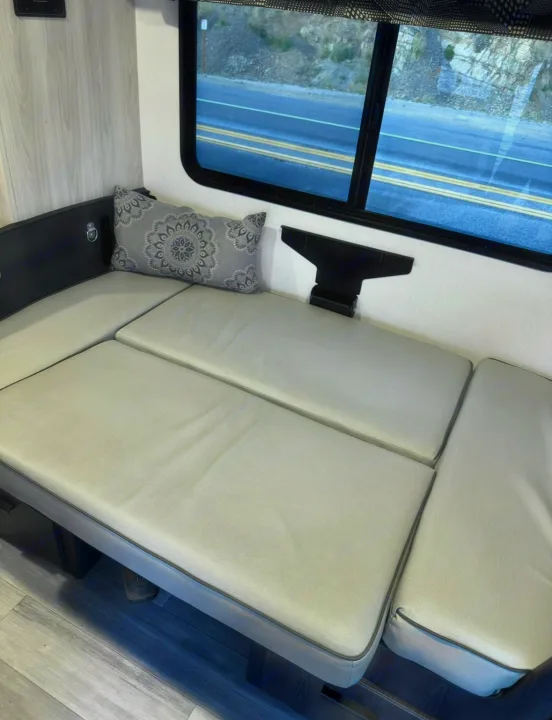 Enjoy this RV rental's comfy bench seating, a decorative pillow, and a scenic road view from the window – ideal for travel.. Forest River Sunseeker LE 2023