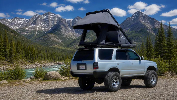 Explore stunning mountain scenery with this silver 4Runner featuring a rooftop tent, perfect for an RV rental adventure by the river.. Toyota 4runner 2001