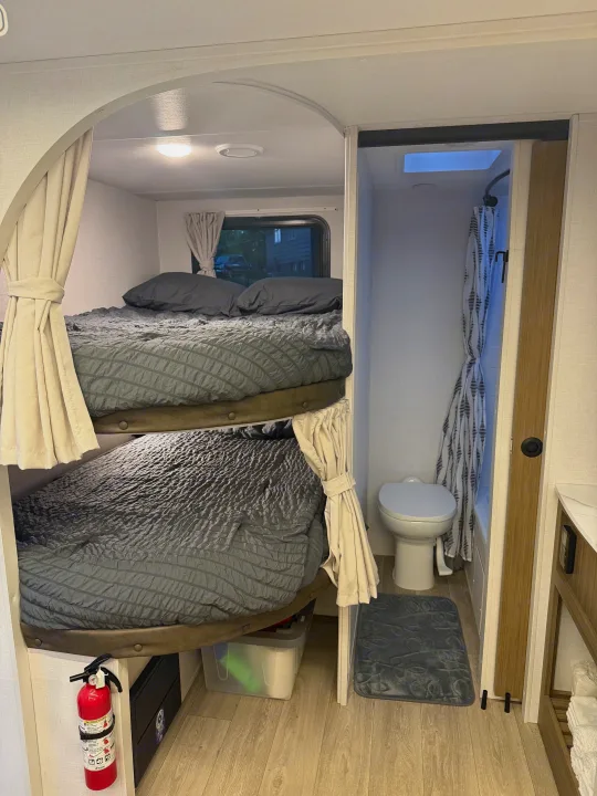 RV rental interior with bunk beds and a compact bathroom, featuring a skylight and a fire extinguisher for safety.. Forest River Wildwood X-Lite 2025