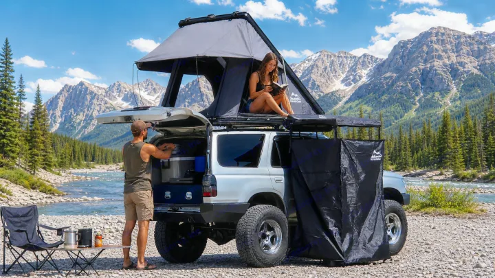 Mountain adventure: couple camping with SUV, rooftop tent & awning by a river. An RV rental-style experience awaits!. Toyota 4runner 2001
