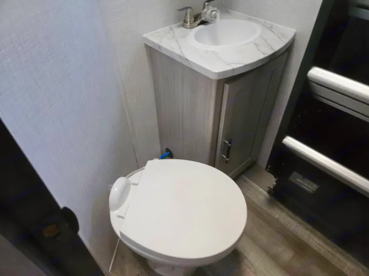 This RV rental features a compact bathroom with a white toilet, corner sink, and light wood vanity. Functional interior design.. Crossroads RV Sunset Trail Super Lite 2025